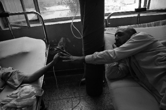 A man passes an oxygen mask to another patient at the Red Crescent Society Hospital, Baghdad, Iraq (2003)
